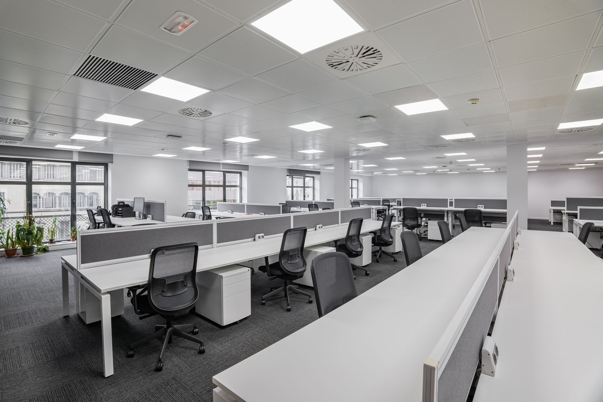 Modern office interior with rows of desks and chairs, white and gray color scheme.