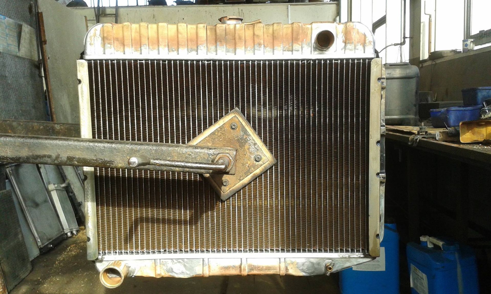 A rusty radiator being cleaned with a tool in a workshop.