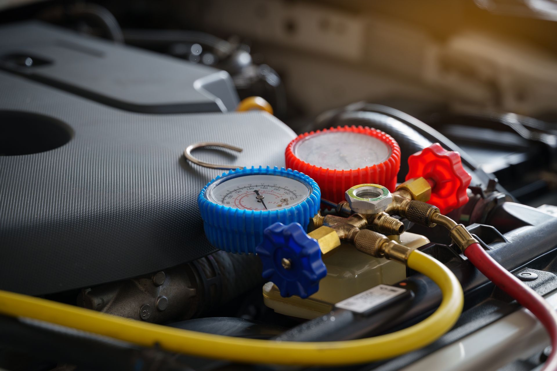 Automotive air conditioning gauges connected to a vehicle's engine compartment, with blue, red, and yellow components.
