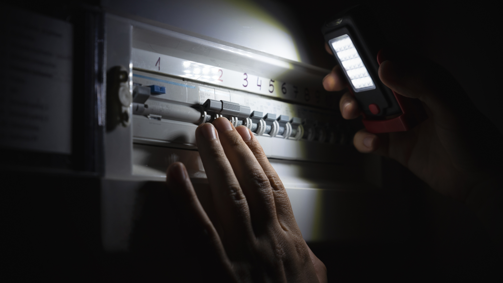 A person is looking at an electrical box with a flashlight.