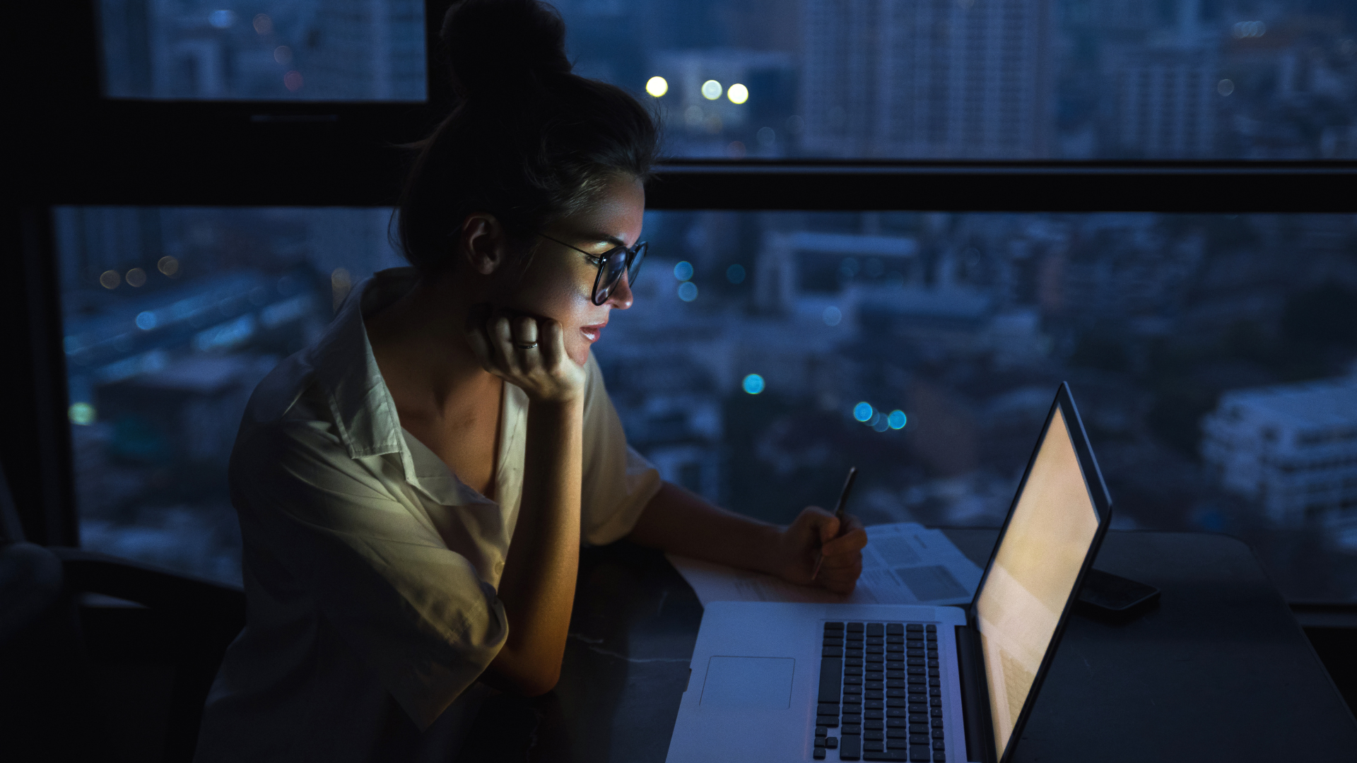 A woman is sitting in front of a laptop computer at night.