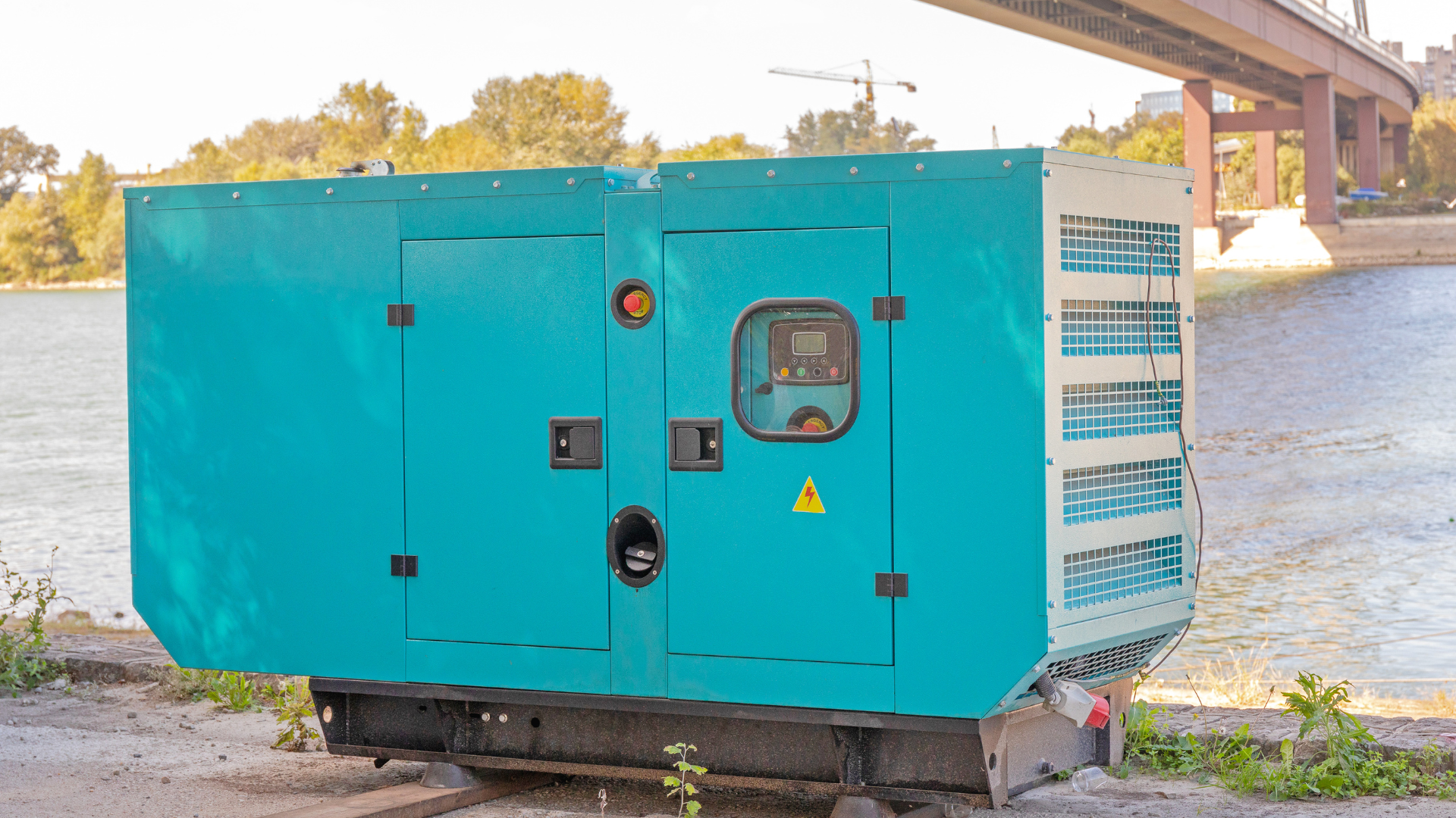 A blue generator is parked on the side of the road next to a river.
