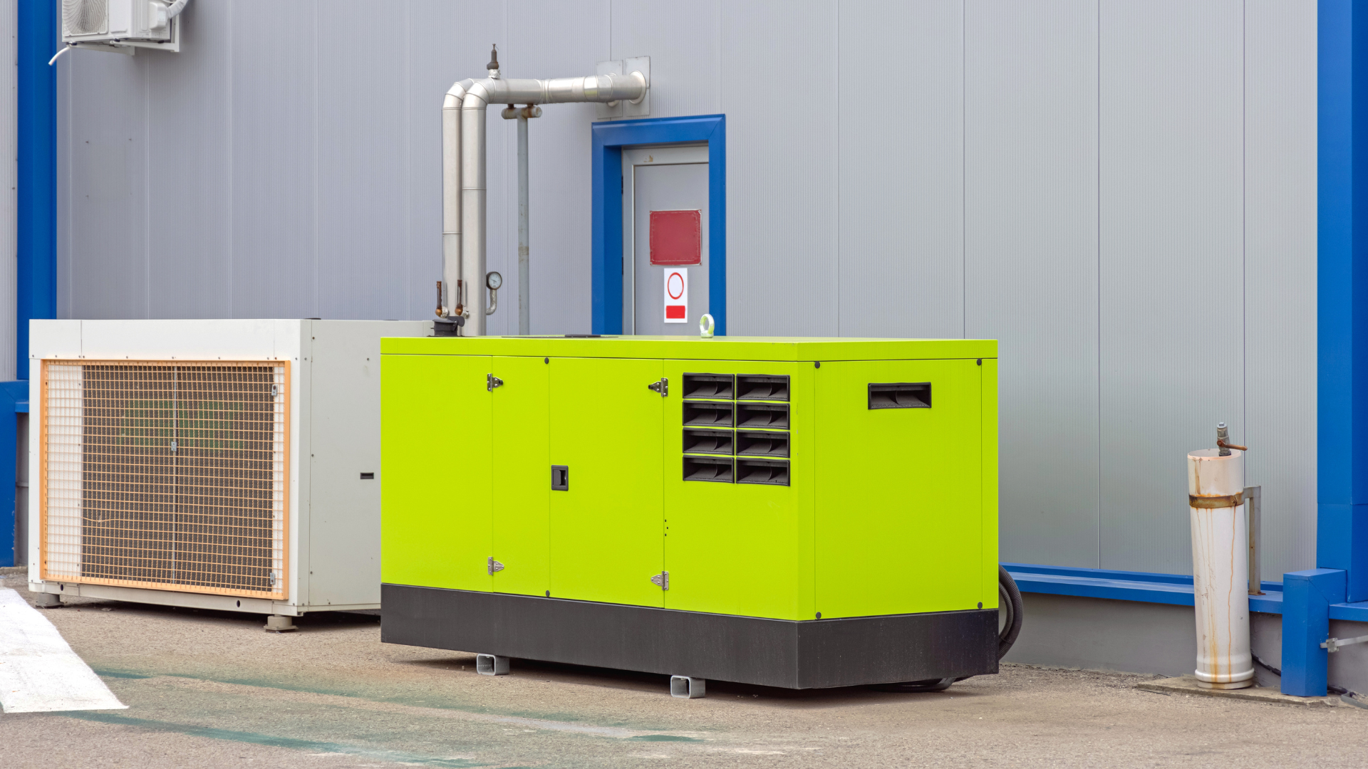 A green generator is parked in front of a building.