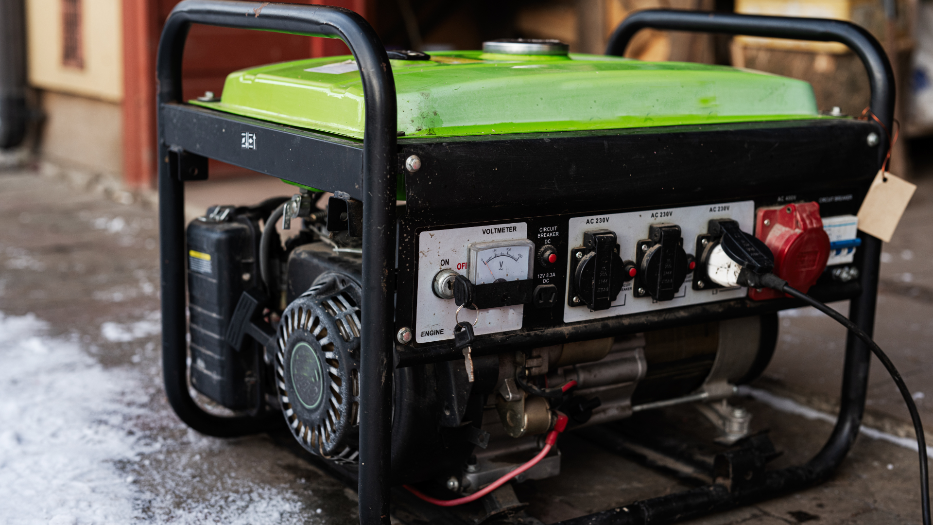 A green portable generator is sitting on the ground outside of a building.