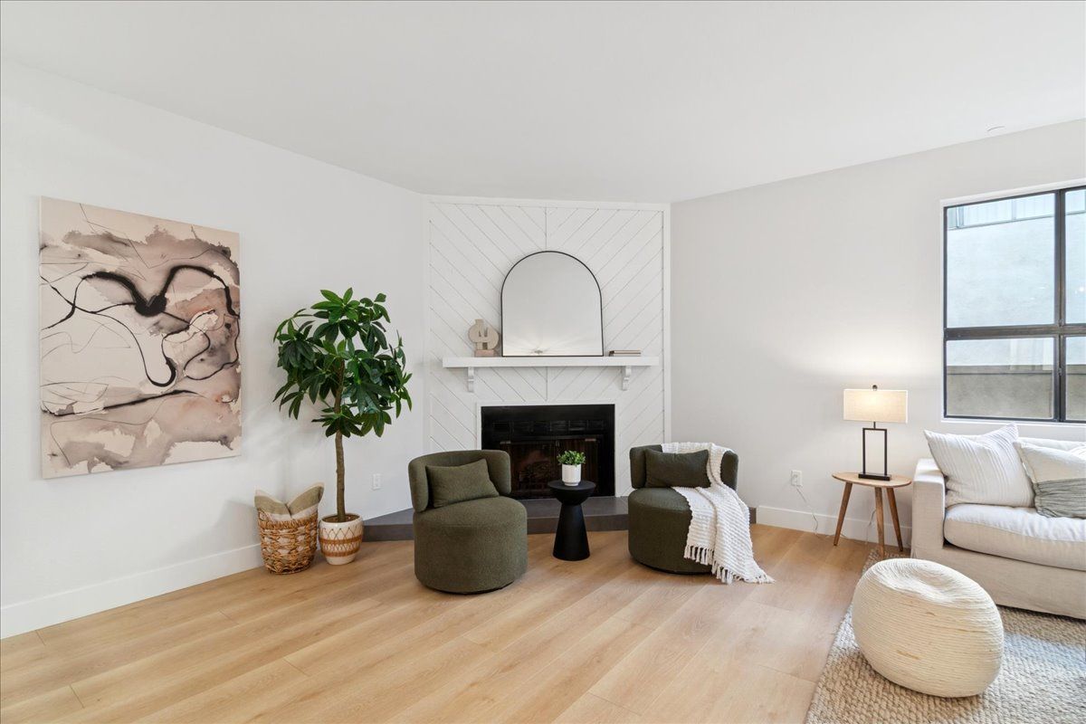 Modern open-concept living space with kitchen island, living room sofa, and staircase. Light wood floors and neutral colors.