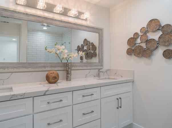 White bathroom with a large mirror, double vanity, and decorative wall art.
