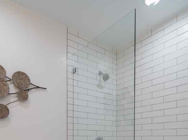 White-tiled shower with glass panel. Showerhead and fixtures visible.
