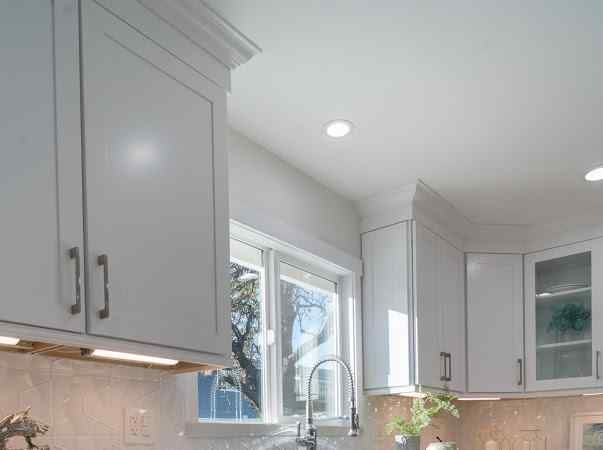 White kitchen cabinets with a window above the sink, lit by recessed ceiling lights.