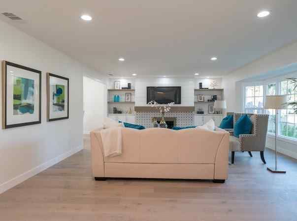 Spacious living room with beige sofa, built-in shelves, and artwork. Bright with wood floors.