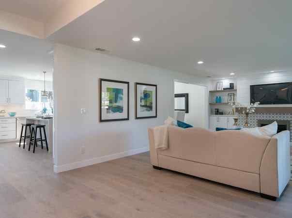 A light-filled living room with a beige sofa, art, and a glimpse into the kitchen.