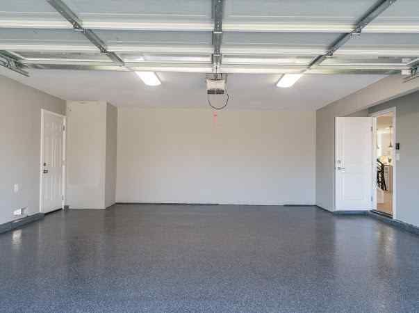 Empty garage with epoxy floor, white walls, doors, and overhead lighting.