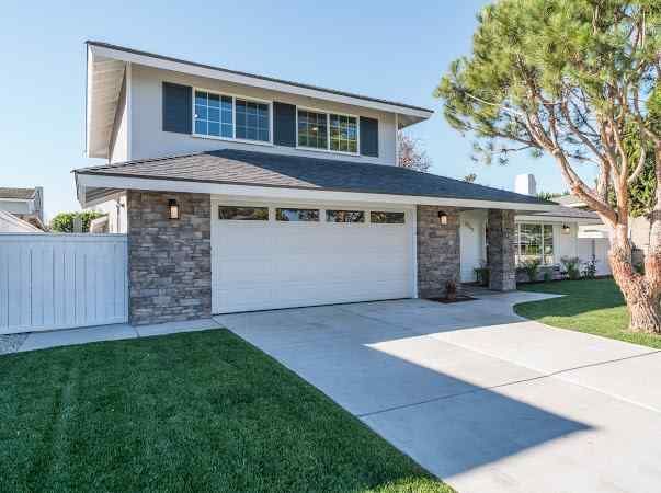Two-story house with gray siding, white garage door, and a green lawn.
