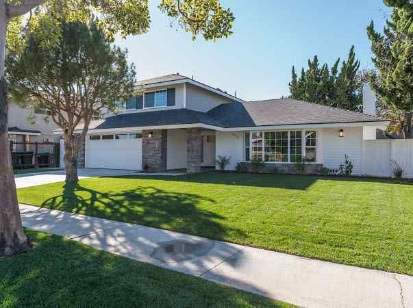 Suburban house with a green lawn, tree, and blue sky. White exterior with a gray roof.