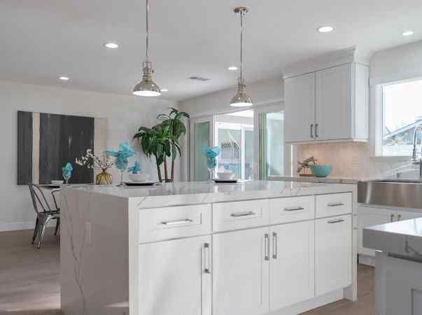 White kitchen with island, cabinets, marble counters, pendant lights, and large windows.