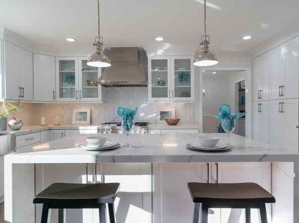 Modern white kitchen with island, pendant lights, and dark stools.