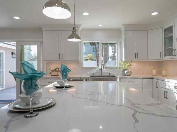 Bright white kitchen with island, cabinets, and marble countertops. Blue napkins and glassware on the island.