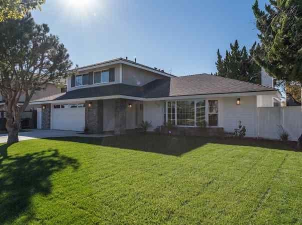 Two-story house with a green lawn on a sunny day. White siding, garage, and front window.