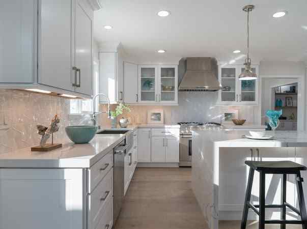 Bright white kitchen with white cabinets, countertops, and island. Stainless steel appliances and a black stool.