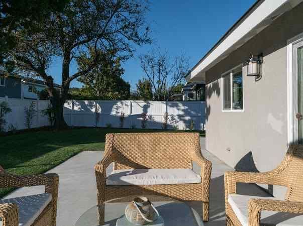 Wicker furniture on a patio; green lawn and white fence in the backyard under a blue sky.