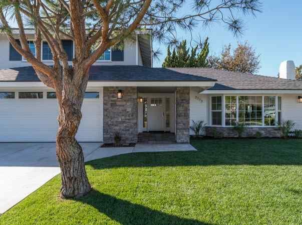 Two-story house with a white exterior, gray roof, and green lawn, with a tree in front.