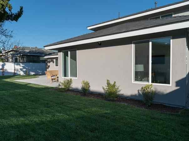 Backyard of a house with gray siding, windows, and green lawn.