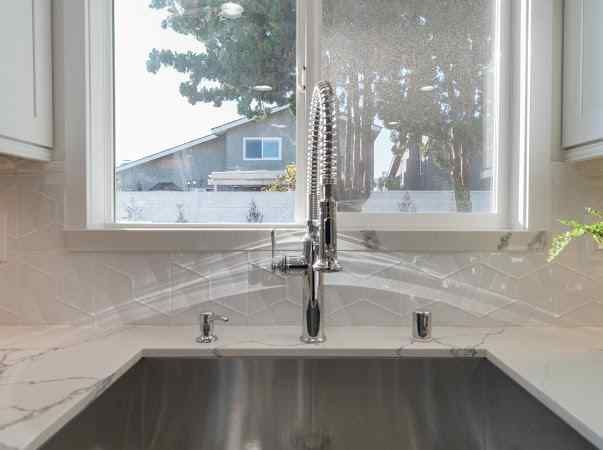 Stainless steel kitchen sink with faucet against a window, showcasing the outside view of a house.
