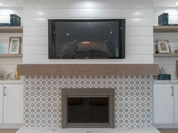 Fireplace with tile surround, TV, wooden mantel, and built-in shelves with decor.