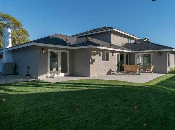 Gray house exterior with patio, lawn, and blue sky.