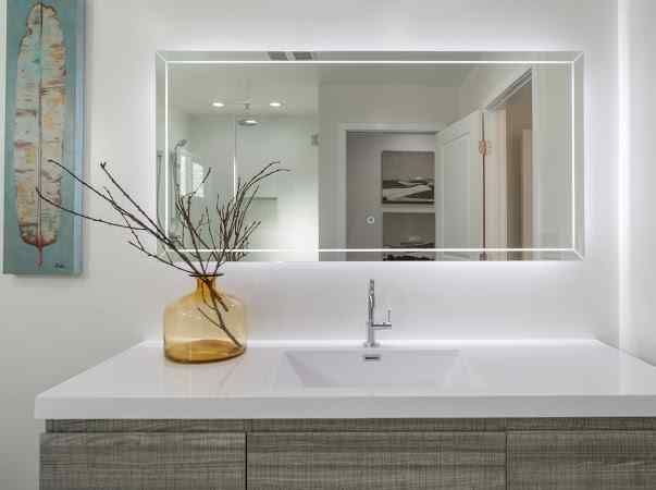 Modern bathroom with a lit mirror over a sink and cabinet; vase with branches.
