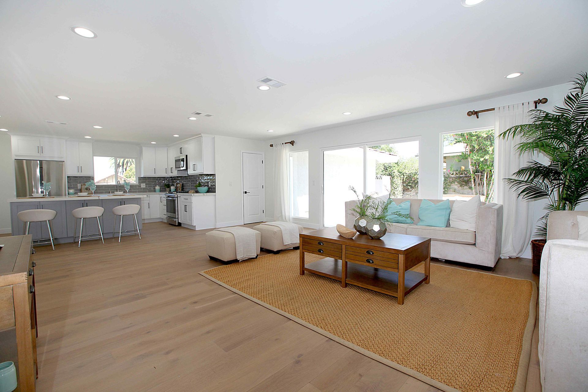 Open-plan living area: kitchen with gray bar stools, seating area with light sofa, wooden coffee table, and sliding glass doors.