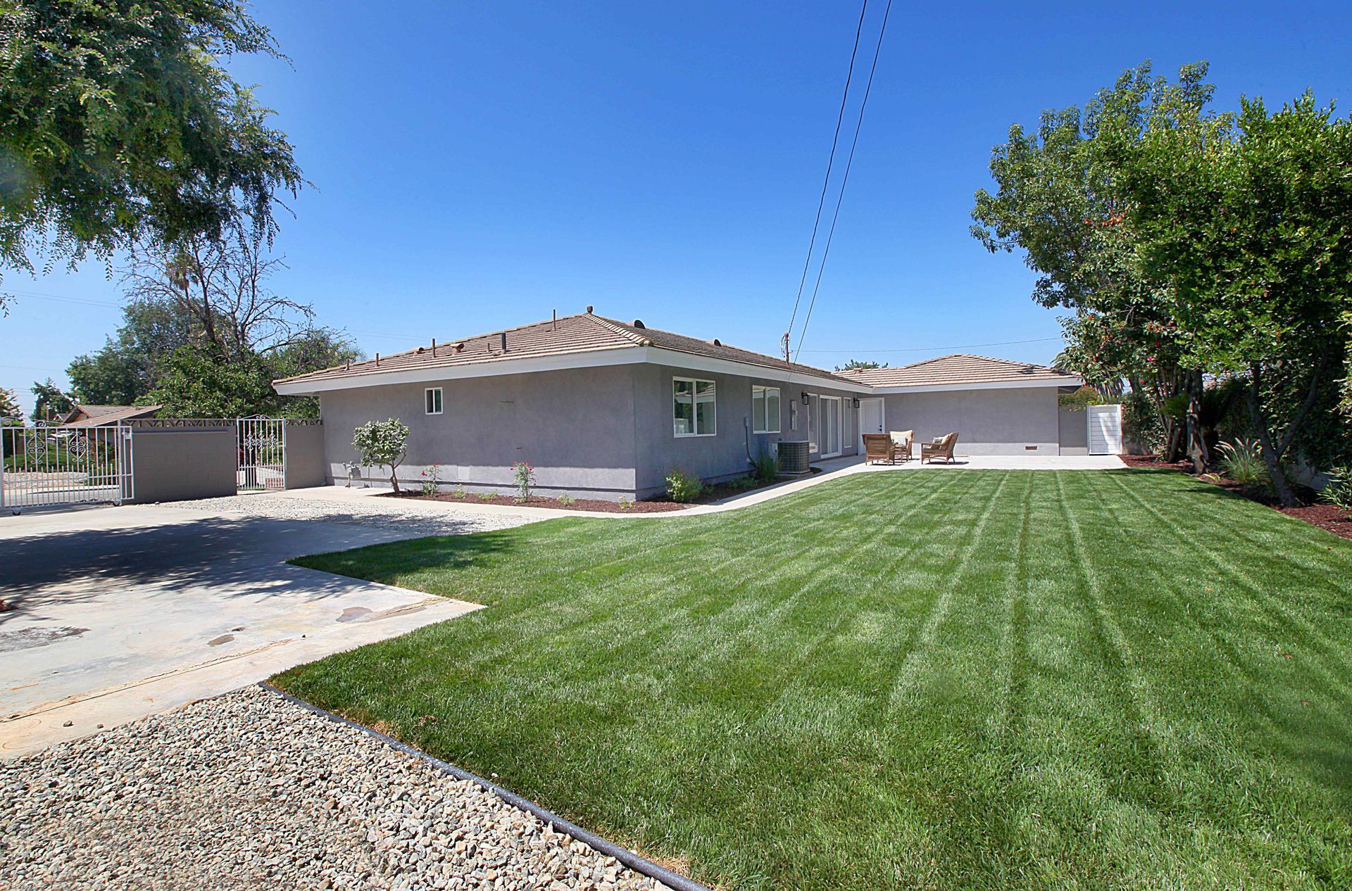 House with a gray exterior, green lawn, and blue sky. A driveway is in front.