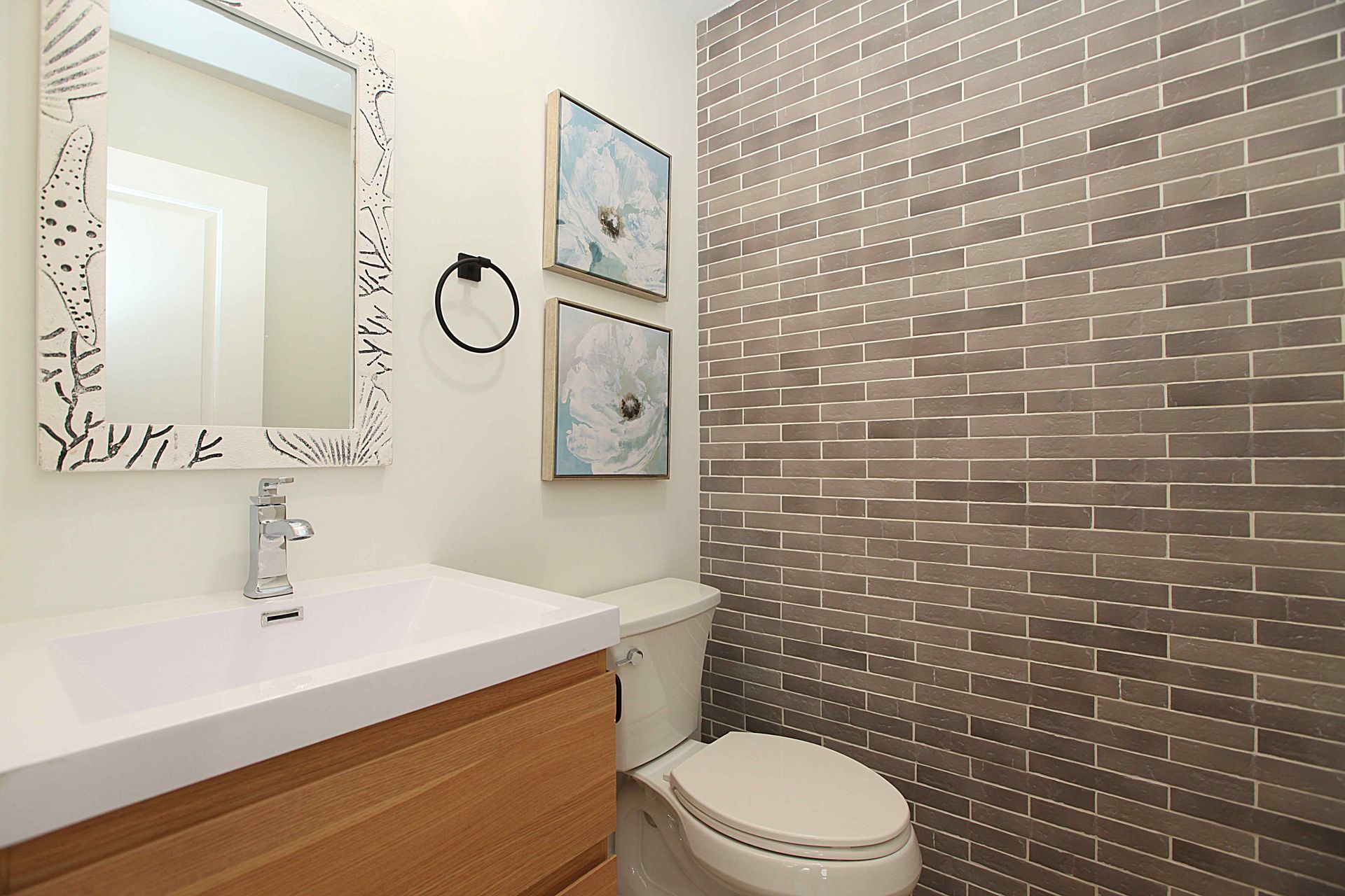 Bathroom with wood vanity, silver-tiled accent wall, white toilet, decorative mirror, and artwork.