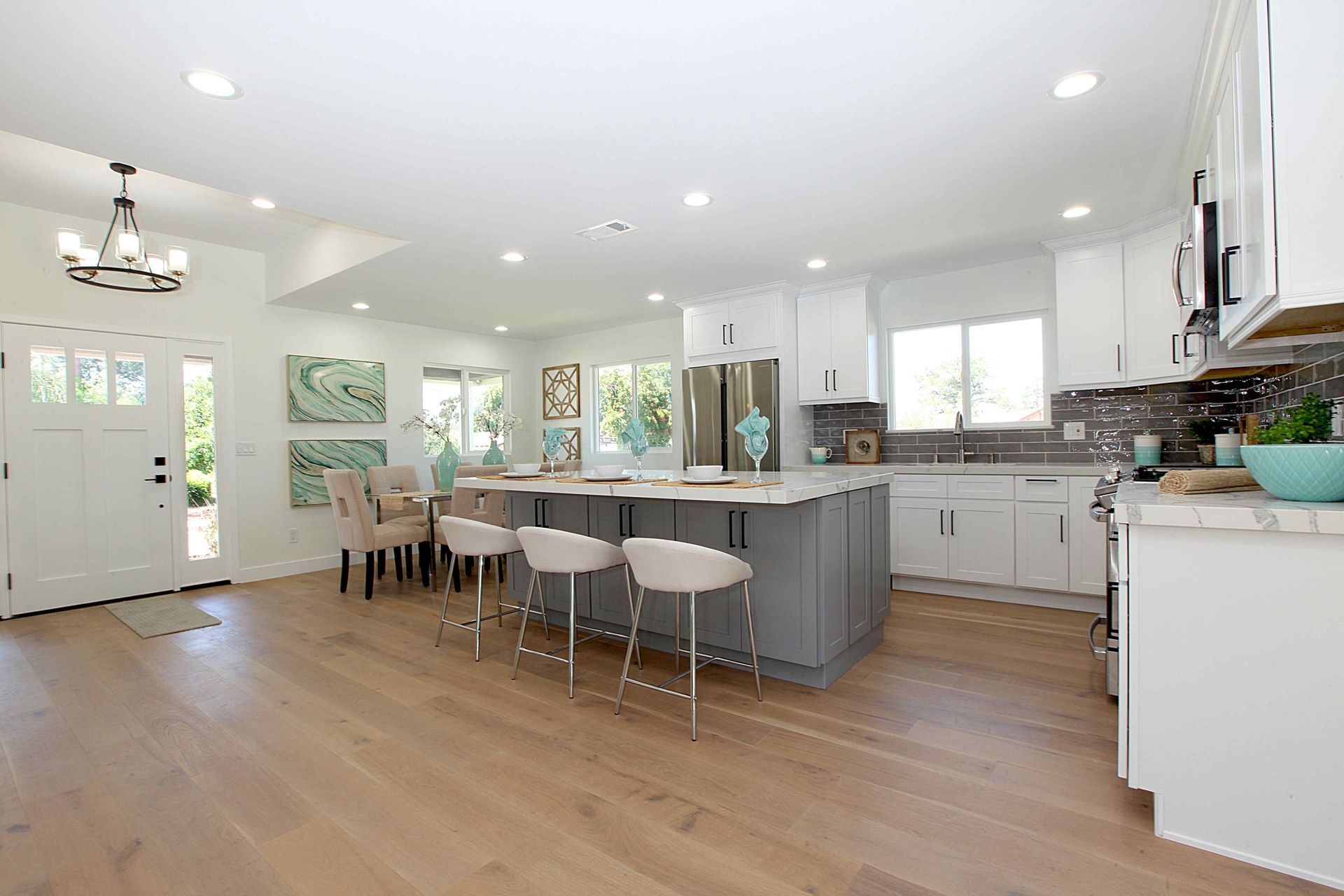 Spacious modern kitchen with white cabinets, gray island, wood floors, and a chandelier.
