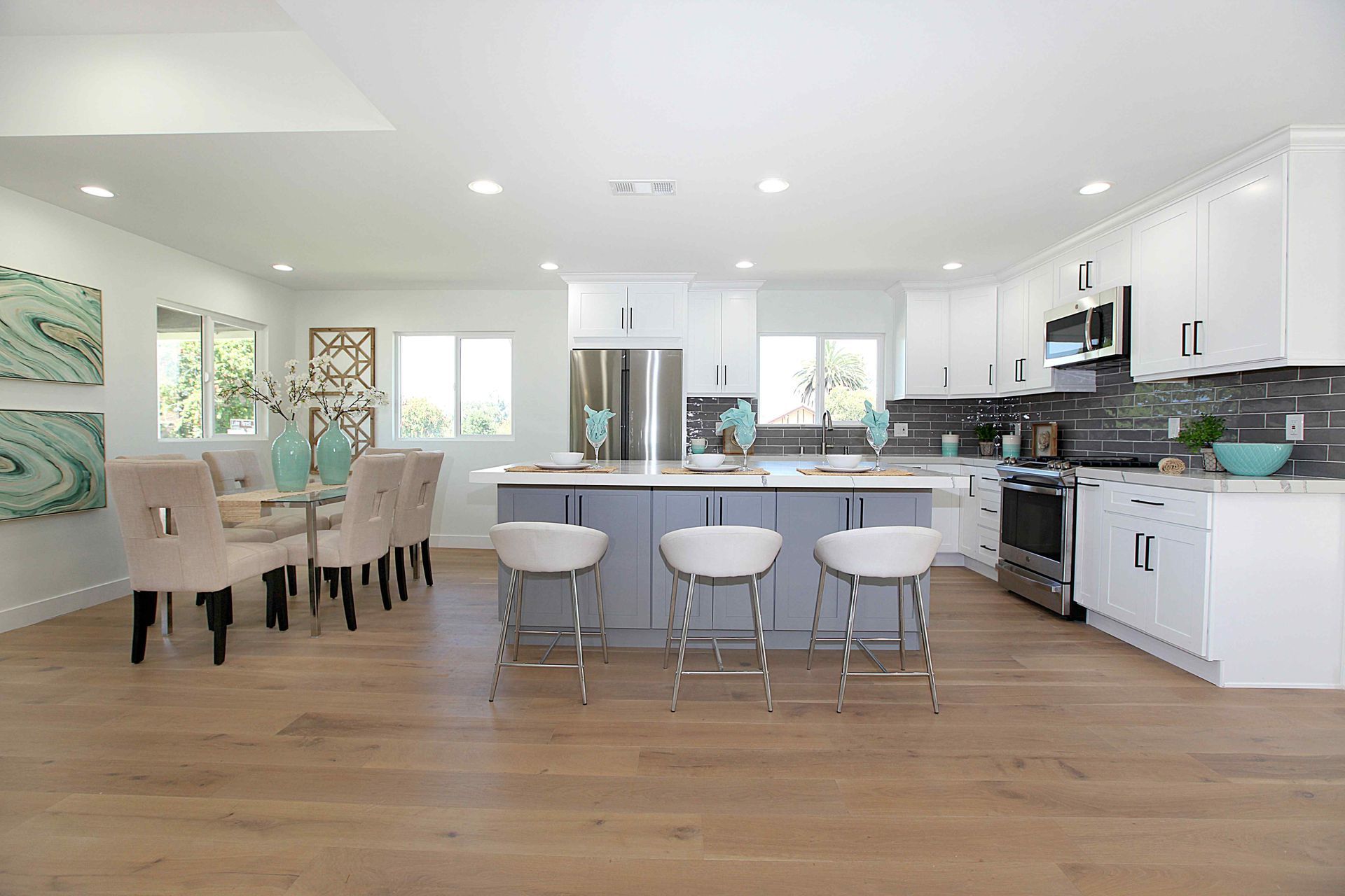 Open-concept kitchen and dining area with white cabinets, gray island, and light wood floors.