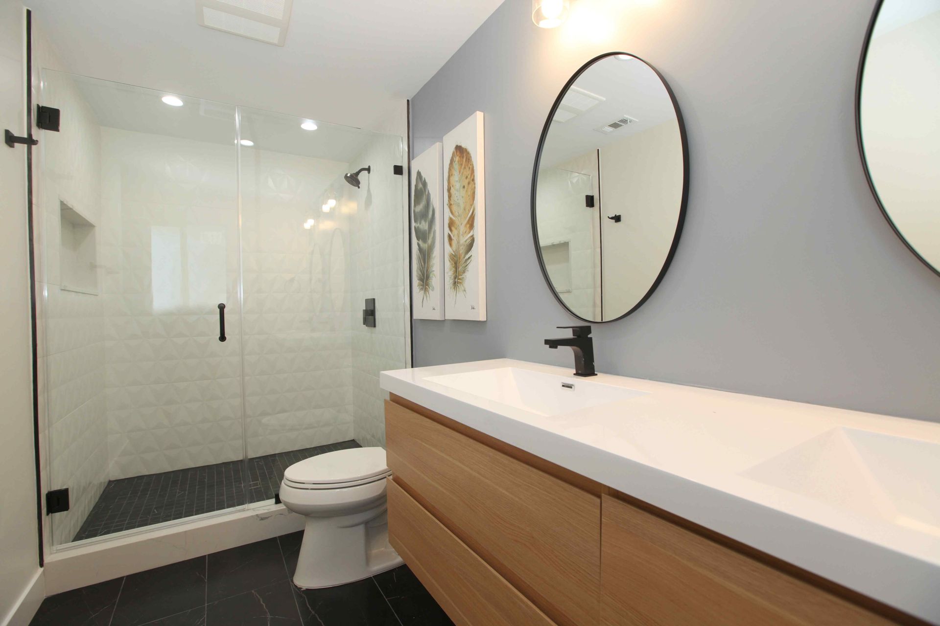 Modern bathroom with a glass shower, vanity, and toilet. Gray and white decor.