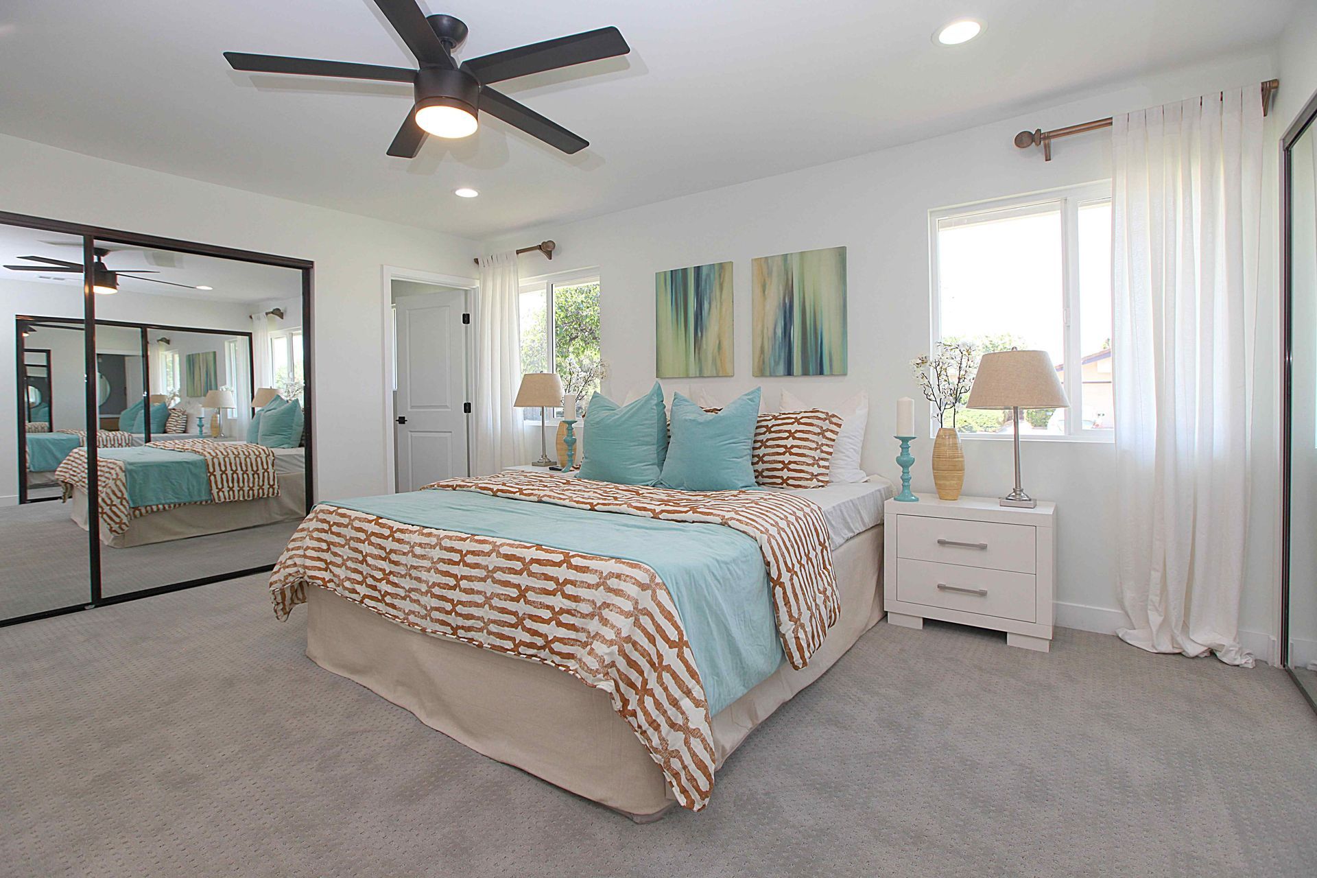 Bedroom with a bed, mirrored closet, windows, and ceiling fan; white walls, blue and gold bedding.