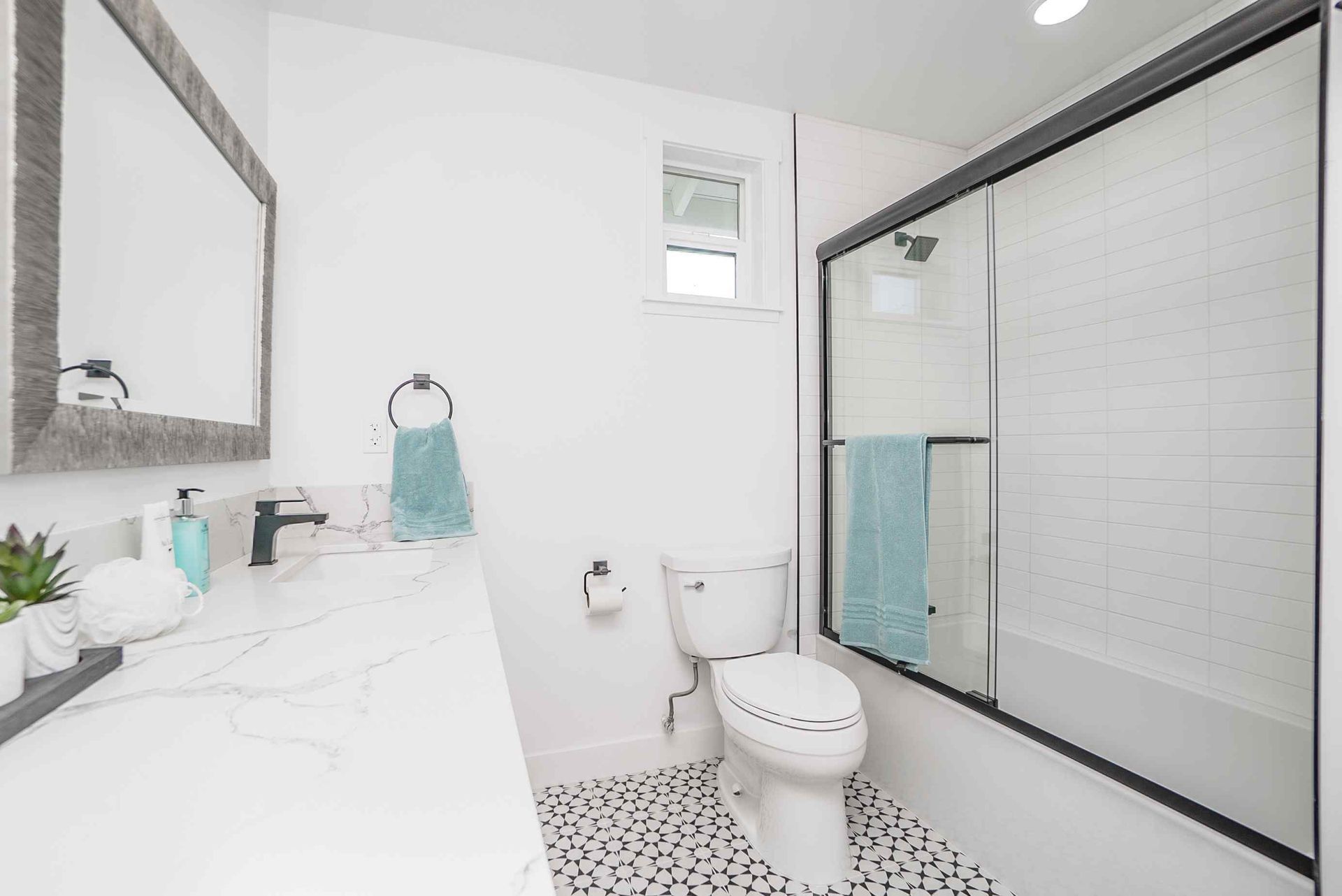 A white bathroom with a black-framed shower, toilet, and vanity with marble countertop.