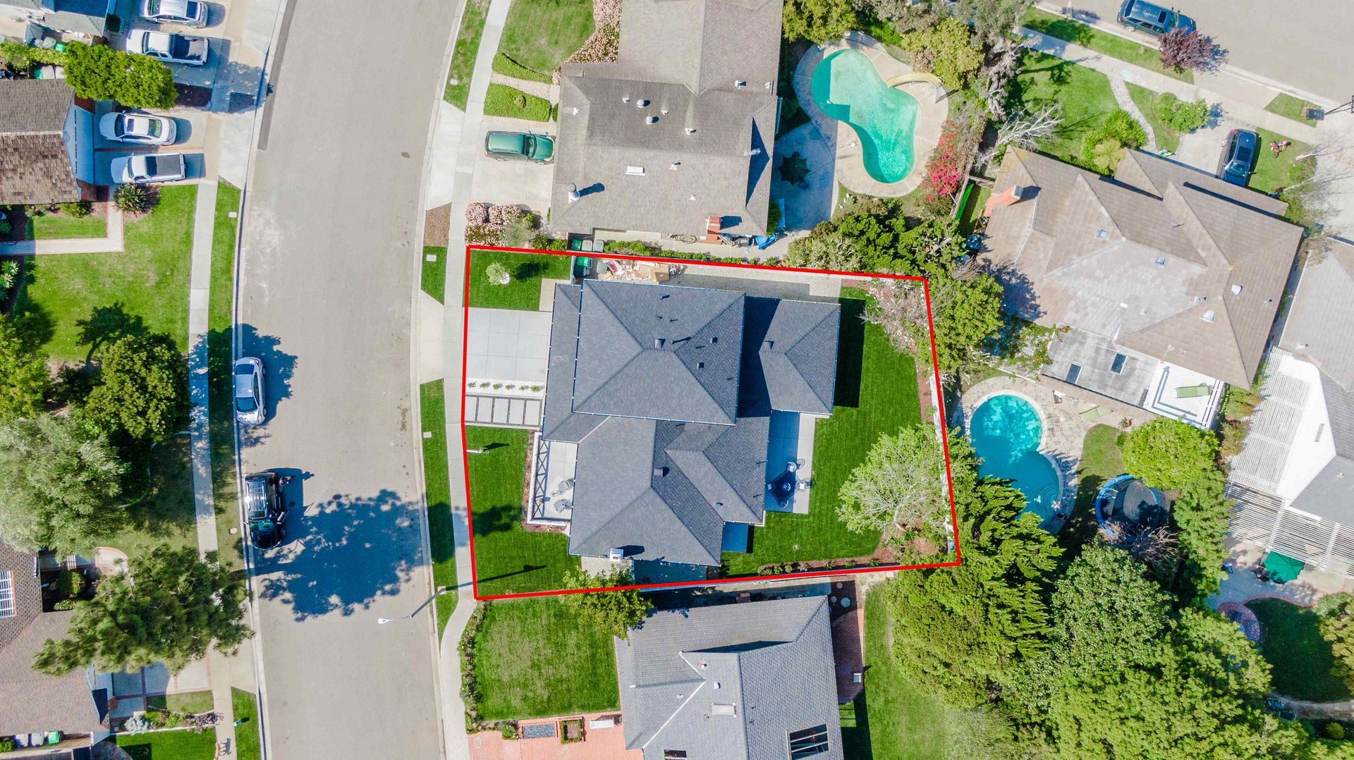 Aerial view of a house with a gray roof, green yard, and red border. Houses and roads surround it.