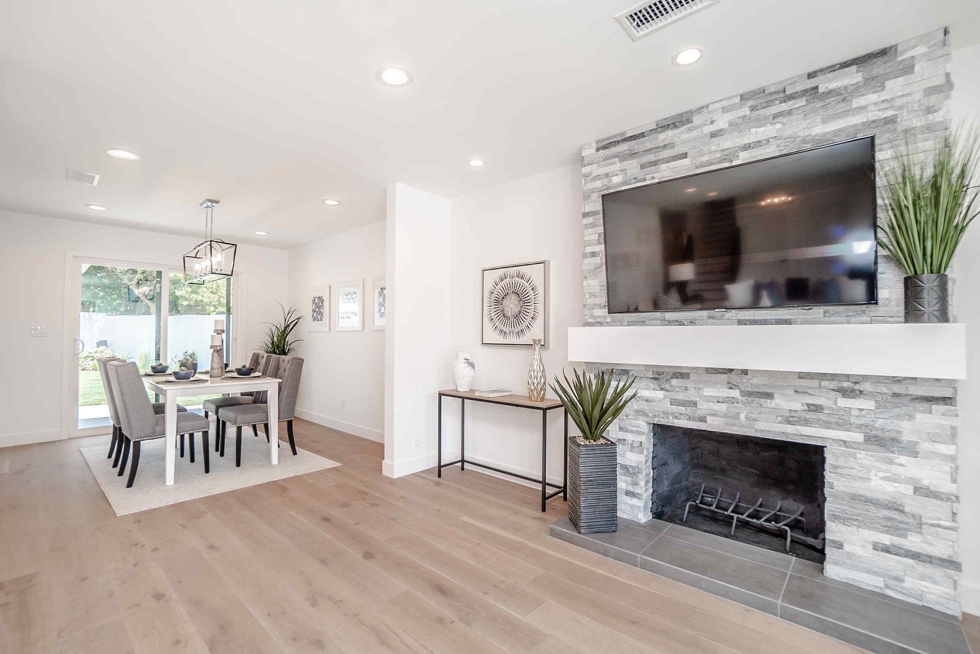 A bright, modern living space with fireplace, TV, dining area, and light wood floors.