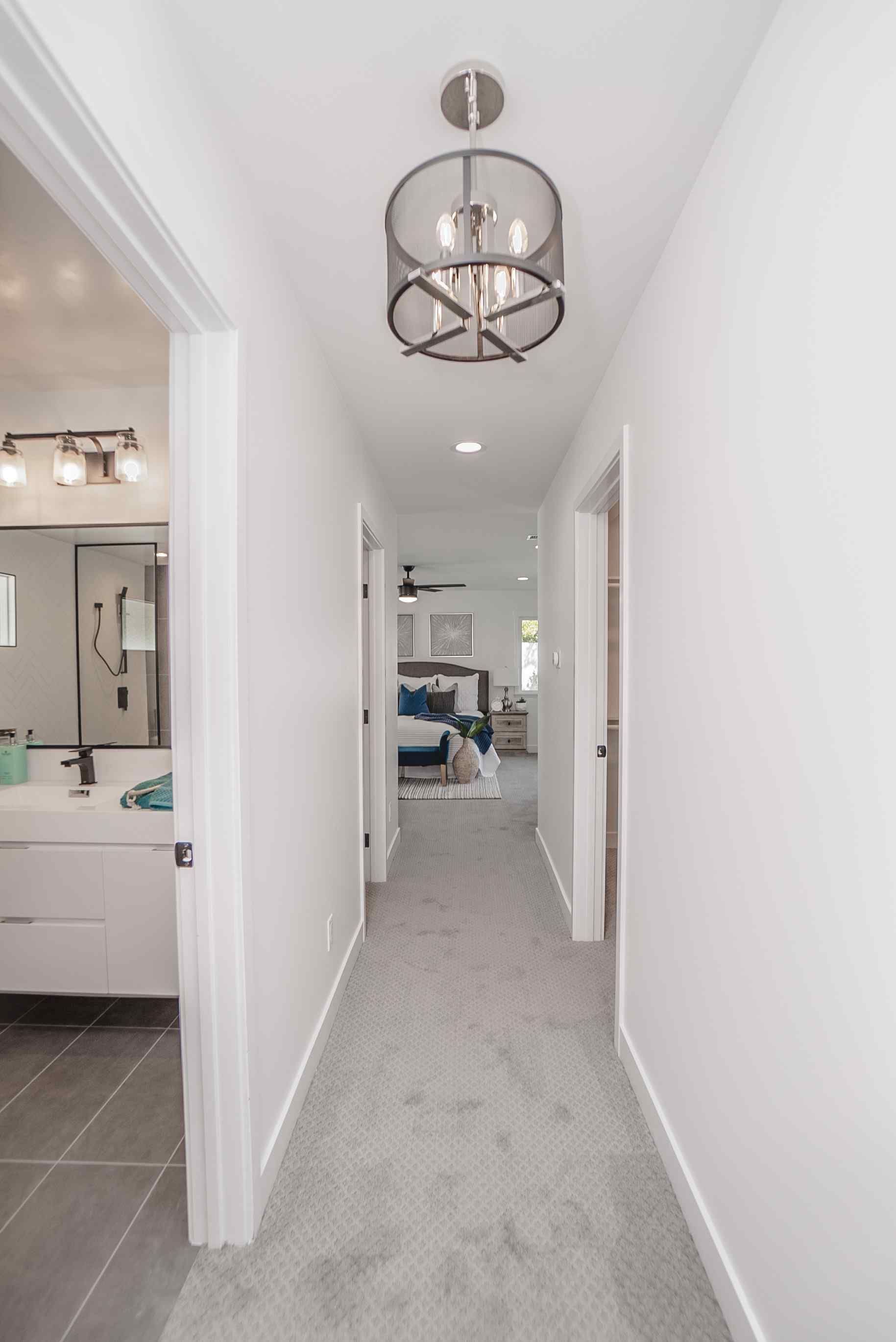 Narrow hallway with white walls, gray carpet, and modern light fixtures.