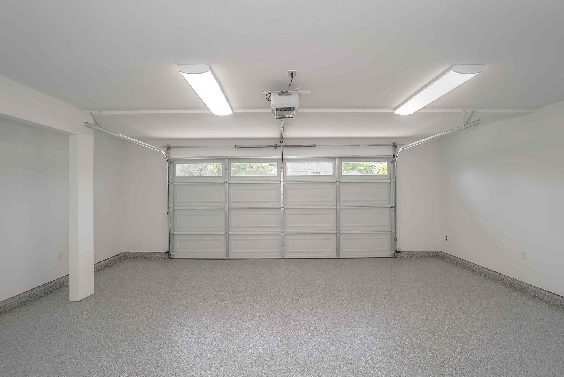 Empty garage with gray speckled floor, white walls, and a closed garage door.