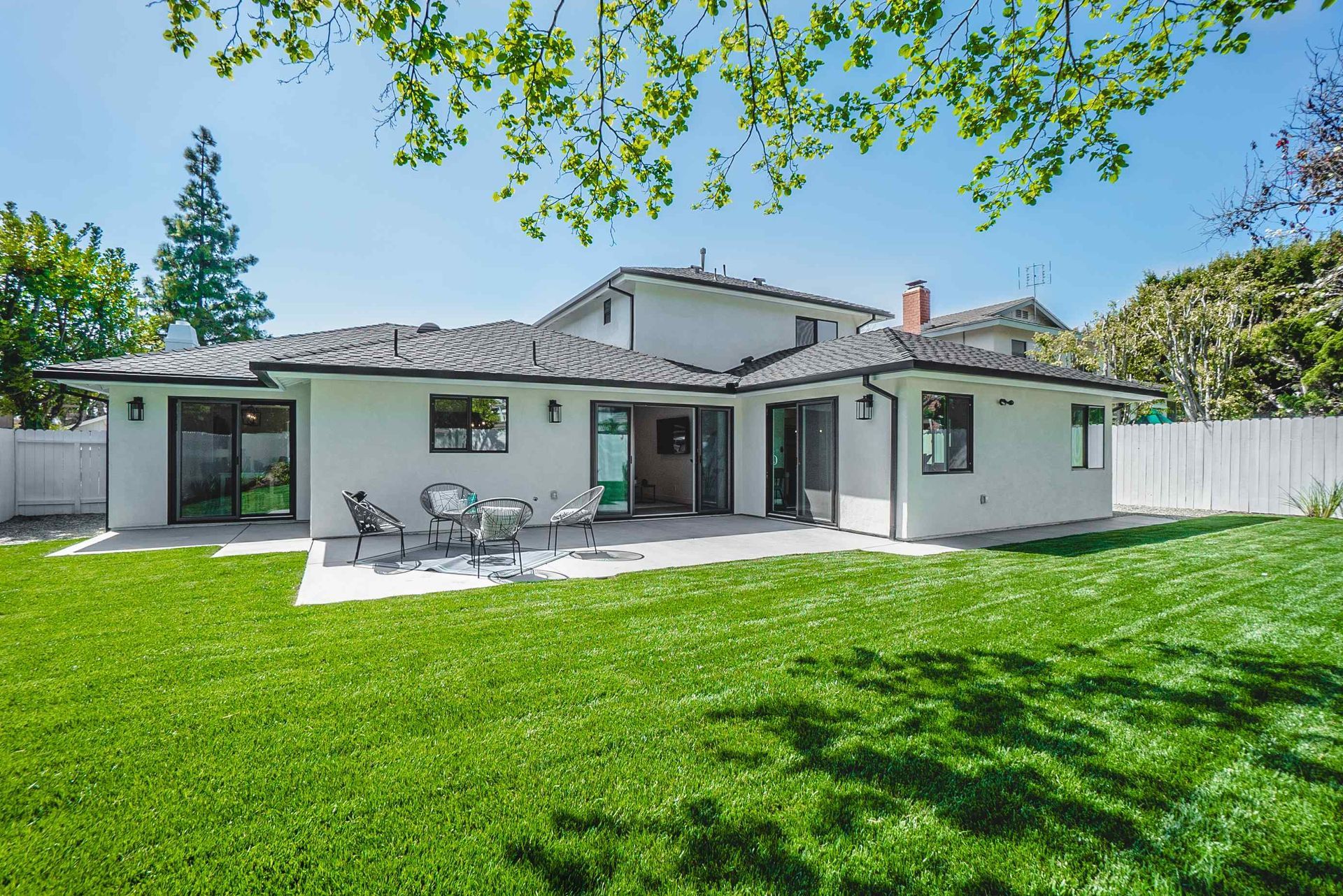 White house with black trim and patio, lush green lawn.