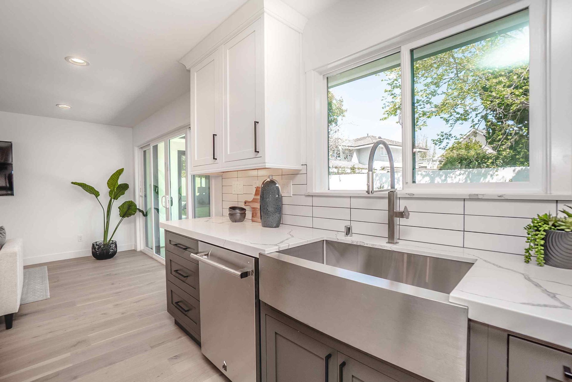 Modern kitchen with stainless steel sink, white and gray cabinets, and a view through a window.