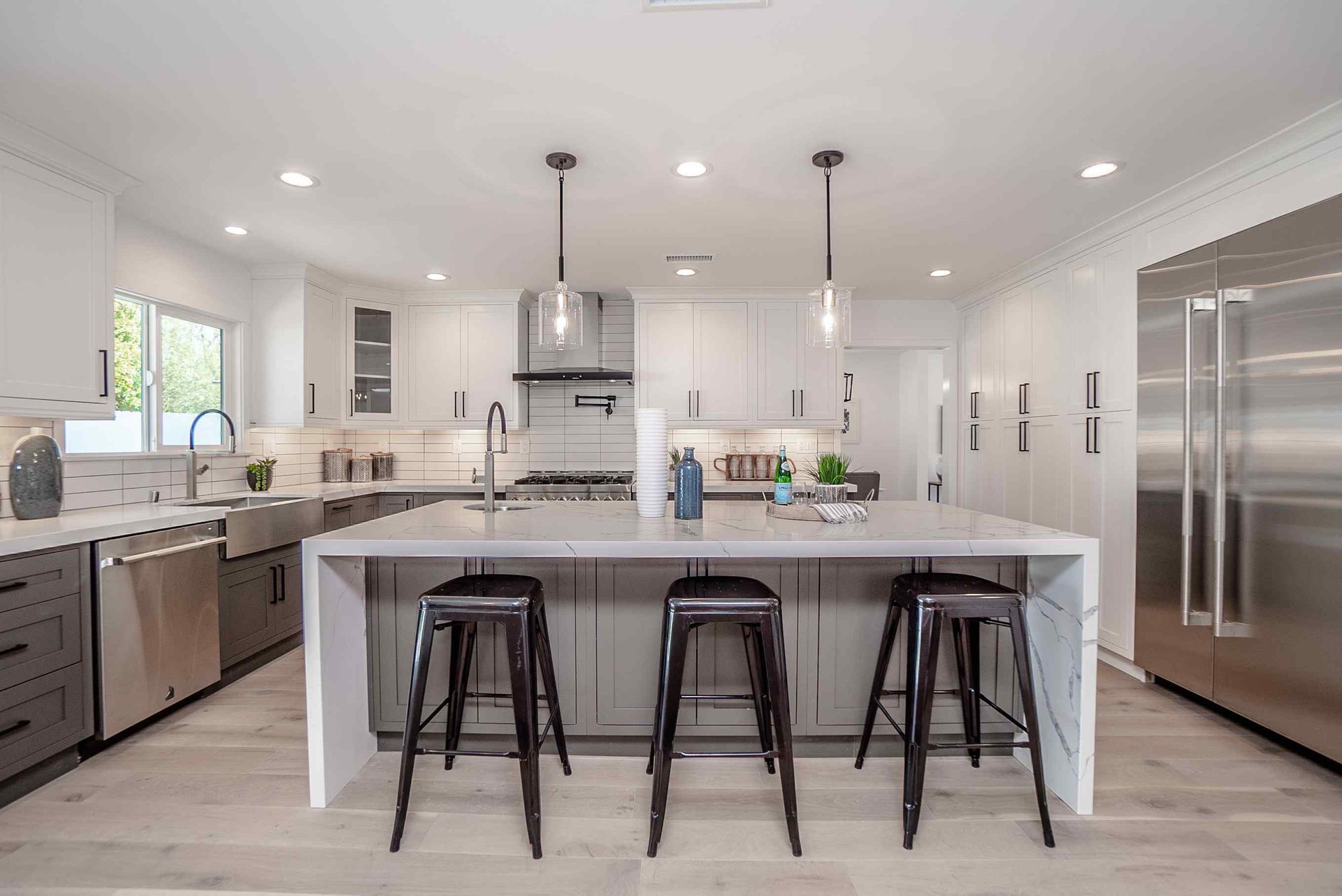 Modern kitchen with a white and gray island, stainless steel appliances, and three black stools.