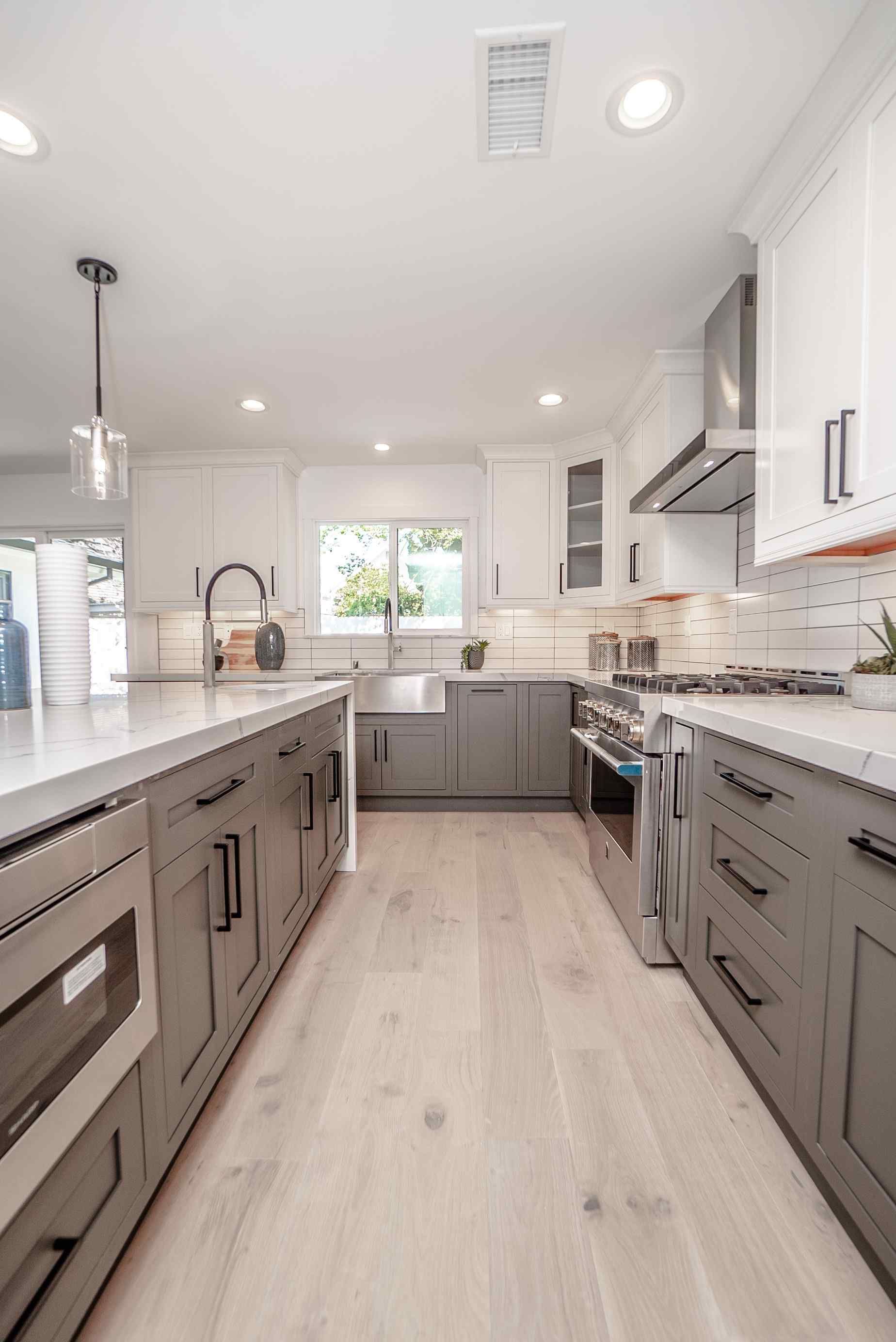 Modern kitchen with gray and white cabinets, light wood floors, and a large island.