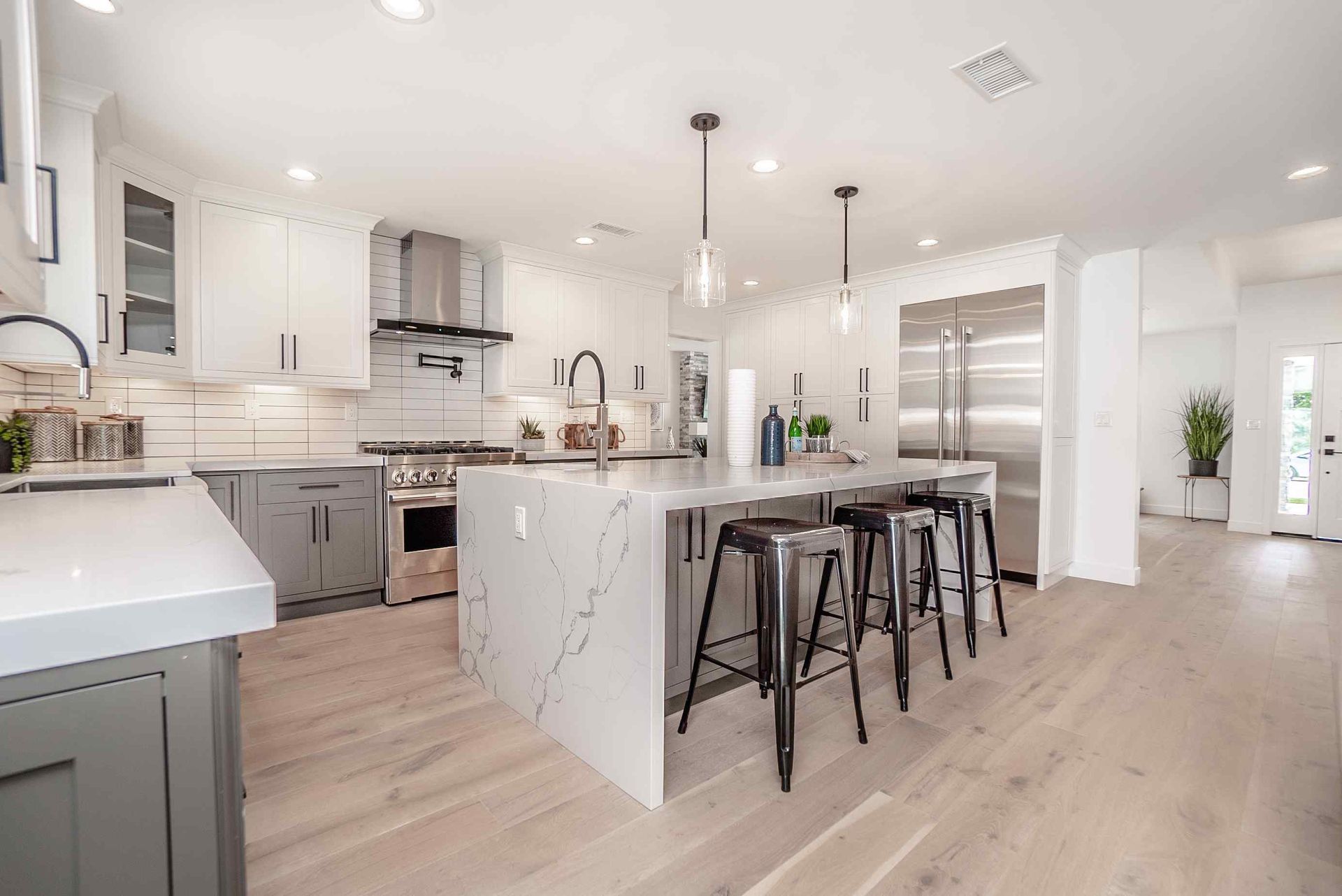 Modern kitchen with white and gray cabinets, island with stools, stainless steel appliances.