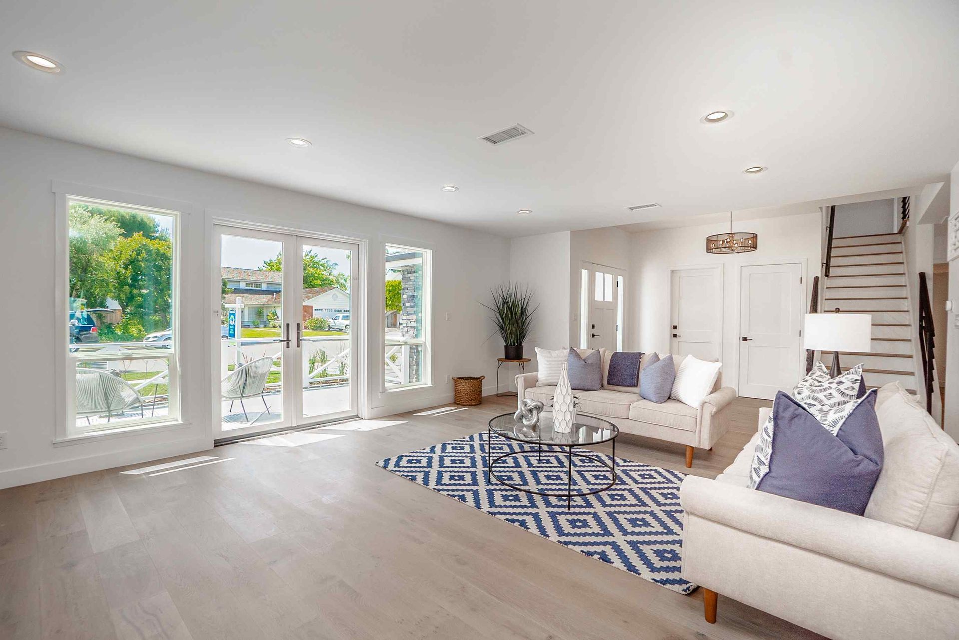 Bright living room with white walls, light wood floors, and blue accent rug; French doors open to the outdoors.
