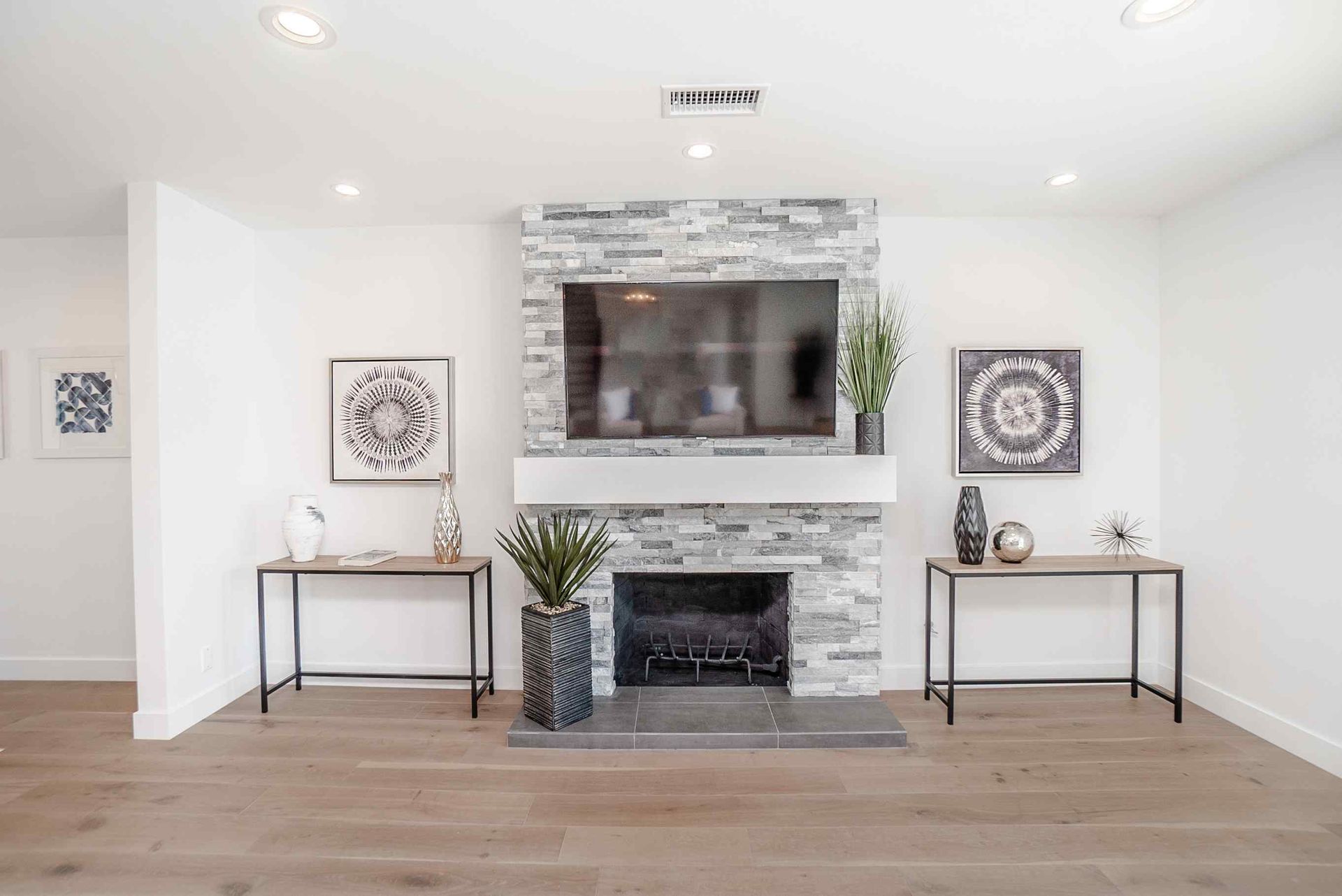 Living room with stone fireplace, TV, and decorative tables with plants and art.