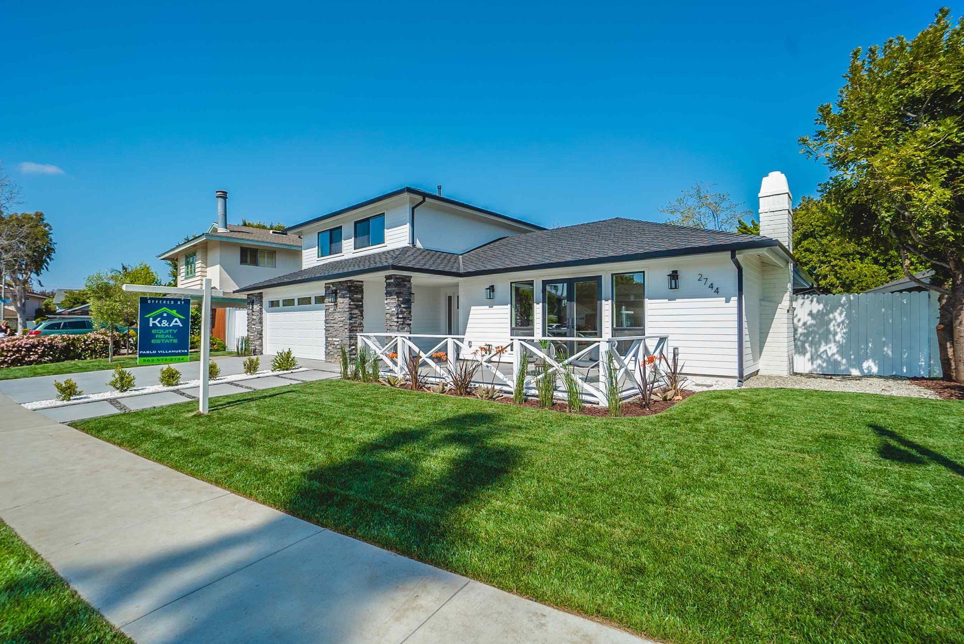 White house with stone accents, green lawn, and a real estate sign. Sunny day.
