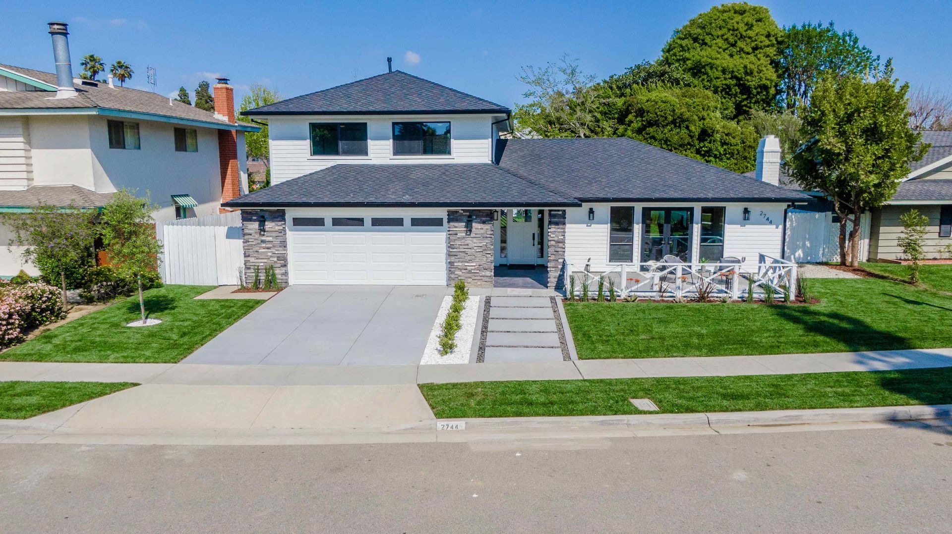 White house with gray roof, stone accents, and green lawn.